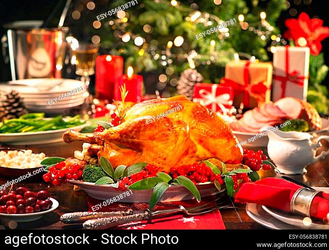 Christmas turkey dinner. Baked turkey garnished with red berries and sage leaves in front of Christmas tree and burning candles