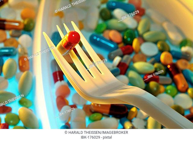 Plastic plate filled with many different colourful pills and capsules, fork with one capsule