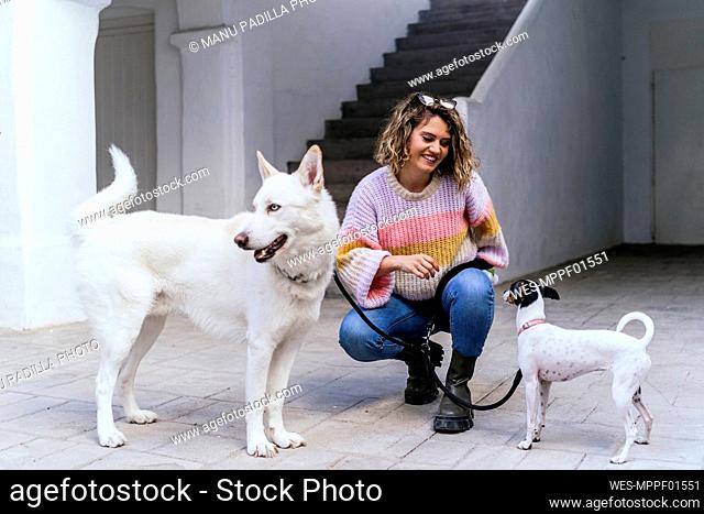 Smiling woman squatting amidst dogs against staircase