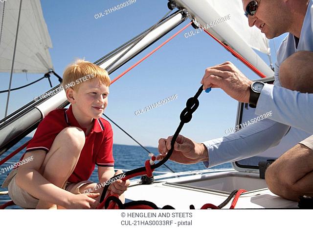 Man teaching boy knot on yacht