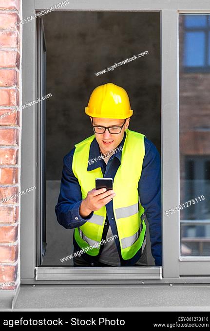 happy male builder with smartphone at open window