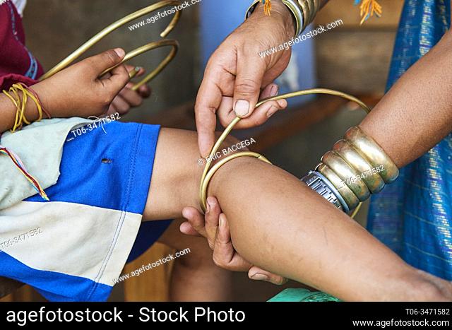 Kayan Lahwi woman putting a brass coil on the lower leg of her daughter. The Long Neck Kayan (also called Padaung in Burmese) are a sub-group of the Karen...