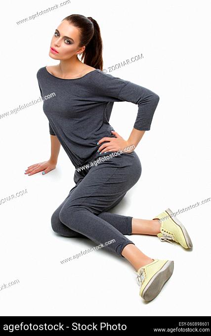 Beautiful active young woman sitting in grey overalls. Isolated over white background. Copy space