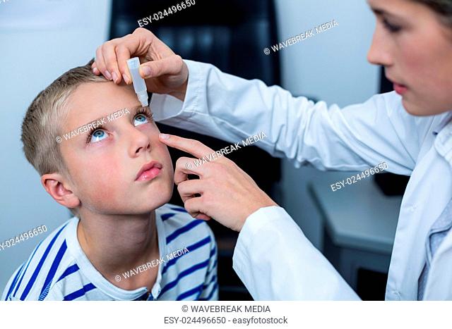 Female optometrist putting eye drop in young patient eyes