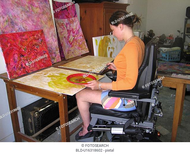 Artist (female wheelchair user) puts paint and brush to canvas in her studio