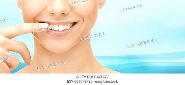 dental health, beauty, hygiene and people concept - close up of smiling woman face pointing to teeth over blue wavy background