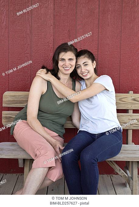 Retrato de sonriente niña caucásica abrazando a la madre en un banco