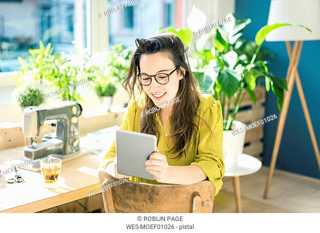 Portrait of smiling fashion designer sitting in her studio using tablet
