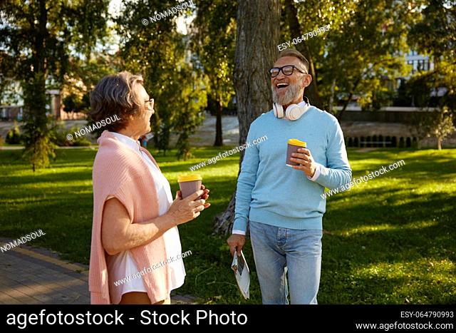 Happy elderly couple having coffee break walking in park. Romantic aged mature man and woman looking happy enjoying healthy lifestyle on pension