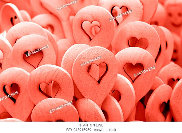 Close up coral pink color toned handmade rustic wooden cooking spoons with carved heart shape at retail market stall display