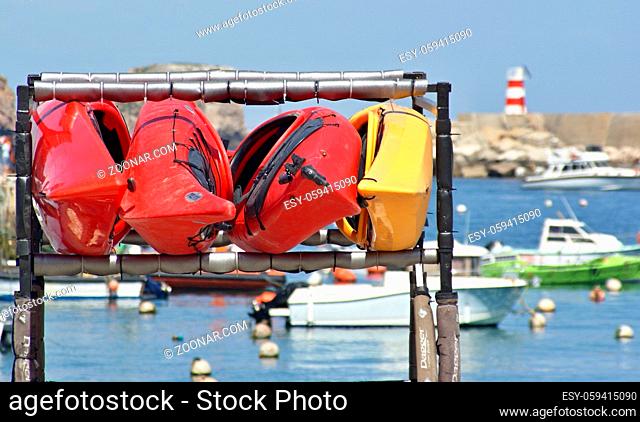 Rote und Gelbe Kanus an einem Staender eingehaengt, dahinter kleine Boote im Hafen von Lagos