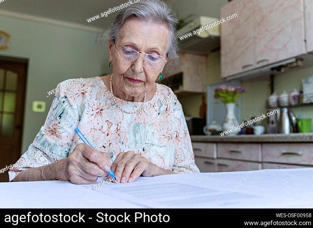 Senior woman with eyeglasses signing home insurance papers on table