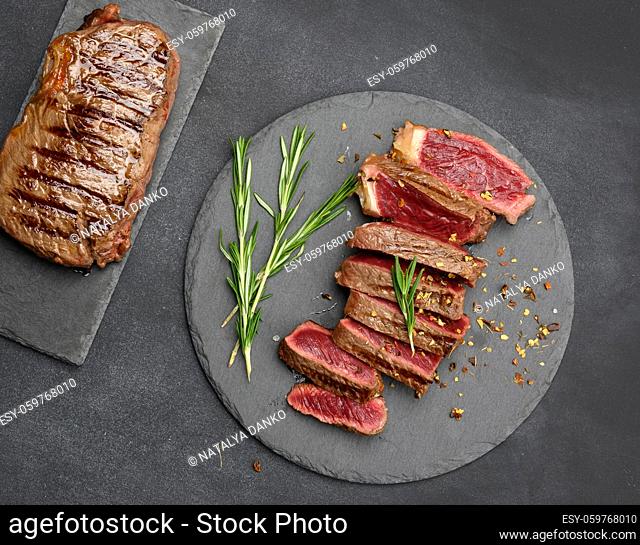 fried beef steaks cut into pieces on a black board, the degree of doneness rare with blood, top view