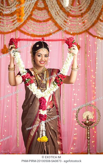 Portrait of a bride in traditional South Indian dress holding a garland and smiling