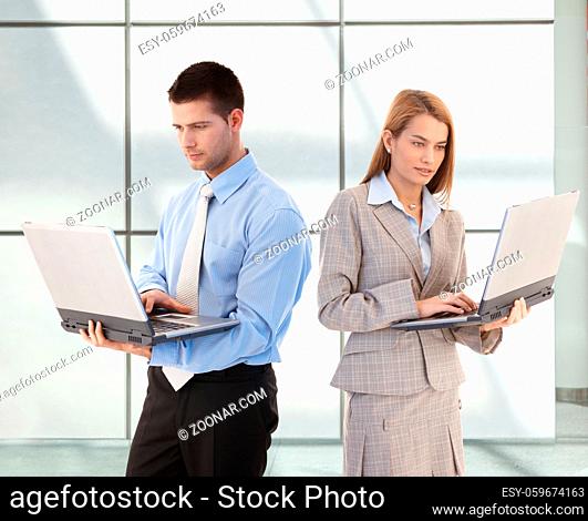 Attractive young businesspeople using laptop in office lobby, standing