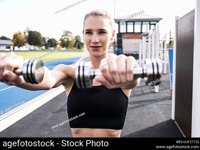 Smiling athlete exercising with dumbbells on sunny day