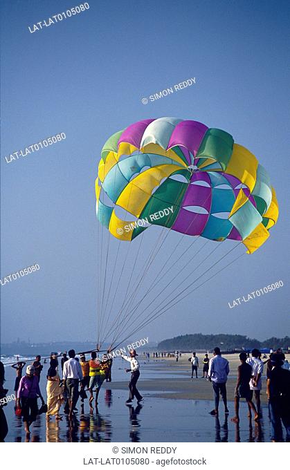 Salcete. Beach, water's edge. Paragliding. Person in harness with parasail in air. People