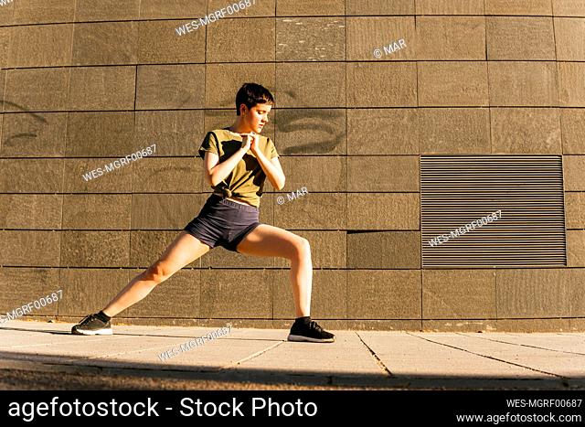Woman exercising in front of wall on sunny day