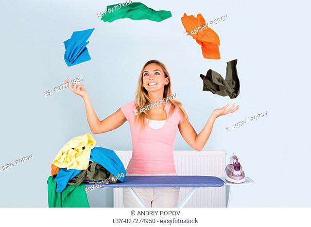 Young Smiling Woman Juggling With Colorful Clothes Near Ironing Board At Home