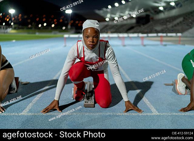 Portrait determined female runner in hijab at track starting line