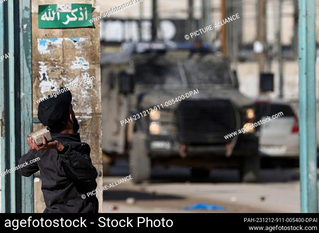 12 December 2023, Palestinian Territories, Jenin: A man throws a stone at an Israeli military vehicle during a raid at the Jenin refugee camp in the occupied...