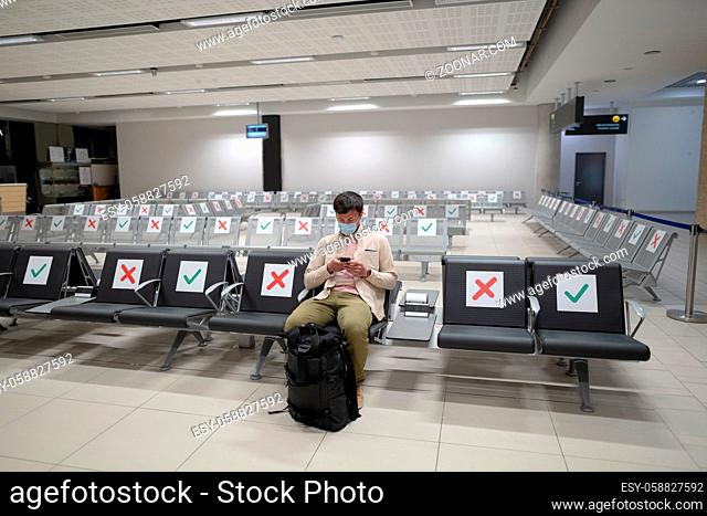 Waiting for flight at empty airport in Cyprus. Man sitting on chair with social distance marker at empty Paphos terminal