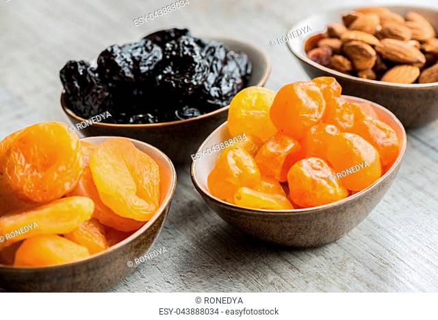 four plates with dried fruits on wooden background: dried mandarins, prunes, apricots and almonds