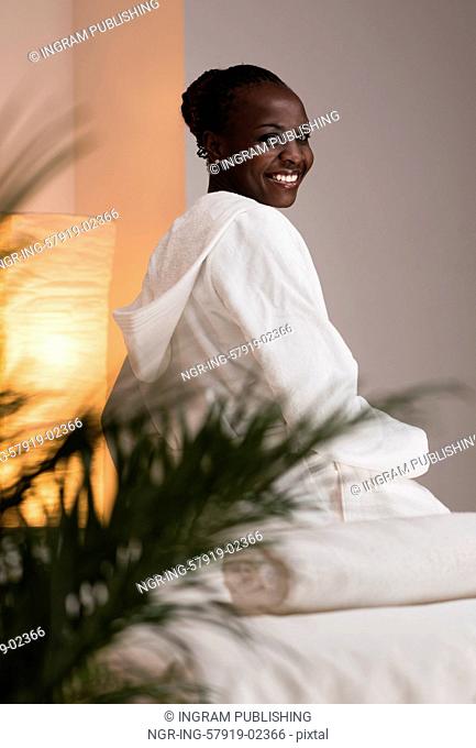 Young pretty african woman sitting at beauty spa salon wearing bathrobe