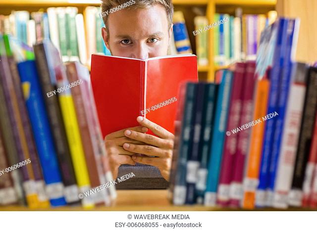 Male student holding book in front of his face in the library