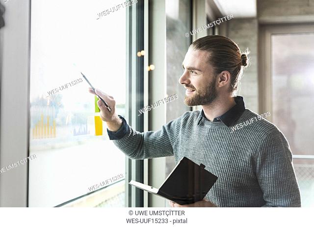Smiling young businessman working on data at windowpane