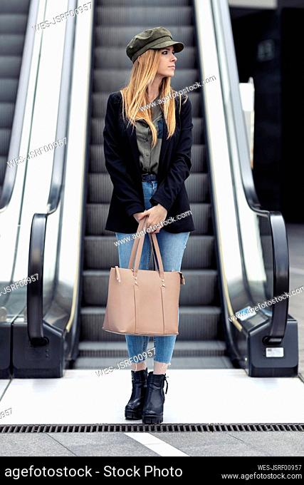 Portrait of blond young woman with bag standing in front on an escalator
