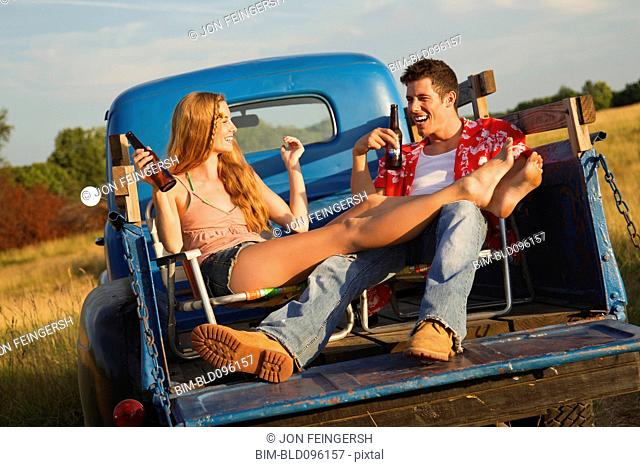 Caucasian couple drinking beer in back of truck