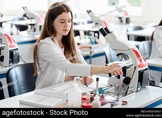 Young female researcher in white coat working in lab with a laboratory sample