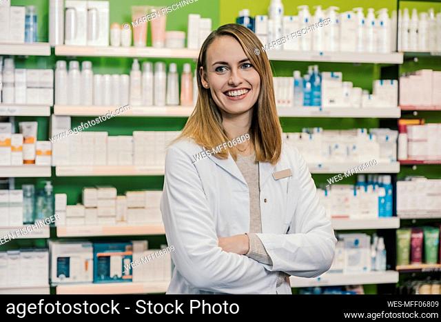 Confident pharmacist with arms crossed looking away while standing in chemist shop