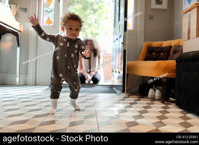 Cute baby girl in star pajamas learning to walk at home