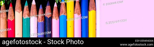 Horizontal wide image bright colour fence made with huge size pencils in row, red, blue, yellow, white, green colors, multi colored wall and green tree lush...