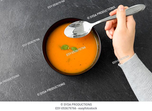 hands with bowl of pumpkin cream soup on table