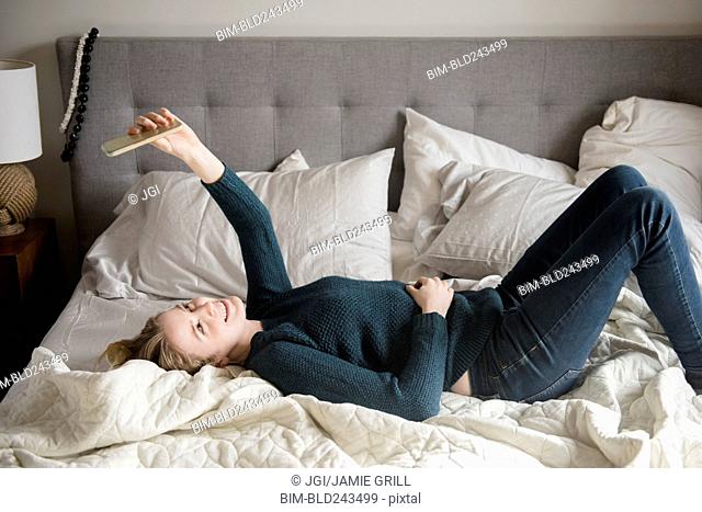 Woman laying on bed posing for cell phone selfie