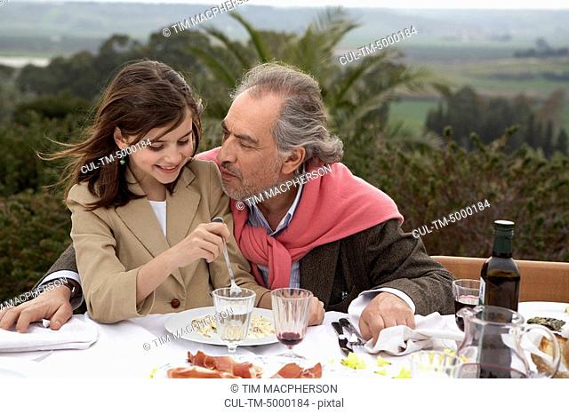 Girl 9-11 sitting with grandfather at a table outside