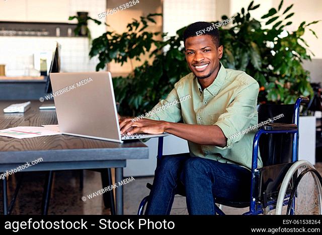 Portrait of smiling african american businessman with disability using laptop in wheelchair