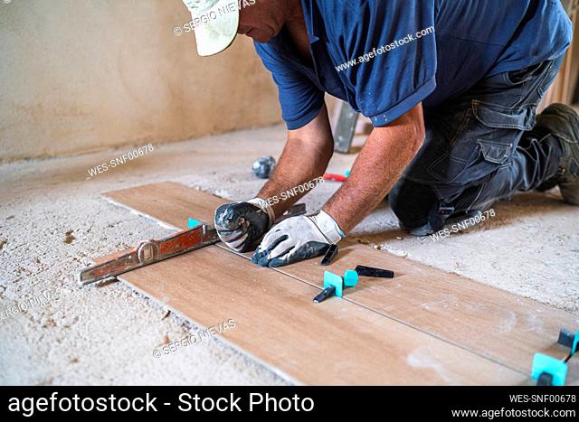 Male manual worker installing parquet flooring in house