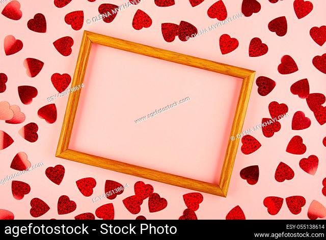 Flat lay view at wooden frame among heart shaped tinsel on pink background