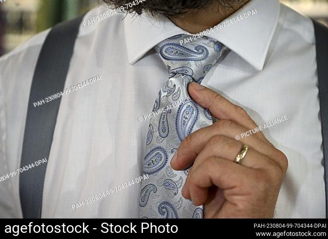 PRODUCTION - 02 August 2023, Berlin: A man wears a tie at the men's outfitter ""Auerbach Manufaktur"". Photo: Jens Kalaene/dpa