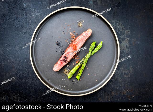 Modern barbecue dry aged wagyu flank steak sliced with green asparagus as top view plate with copy space