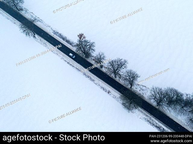 06 December 2023, Mecklenburg-Western Pomerania, Qualitz: A car drives on a cleared road through a snowy winter landscape
