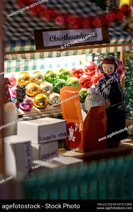 PRODUCTION - 05 December 2023, Bavaria, Coburg: A miniature saleswoman offers Christmas tree baubles for sale at a stand