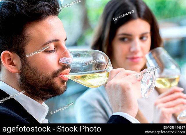 Close up portrait of young man tasting white wine in restaurant next to girlfriend