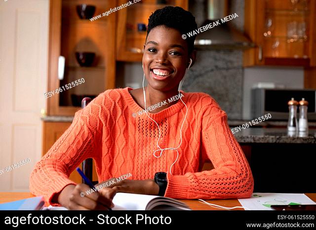 Portrait of african american woman wearing earphones taking notes while working from home