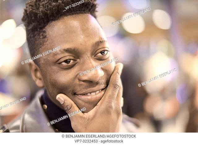 headshot of young smirking man in city lights with positive mindset, African descent, looking aside, thinking about ideas, in Munich, Germany
