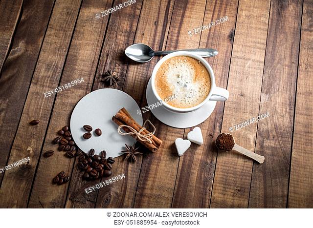 Coffee and spices. Coffee cup, cinnamon sticks, coffee beans, anise, sugar, spoon and beer coasters on wood table background